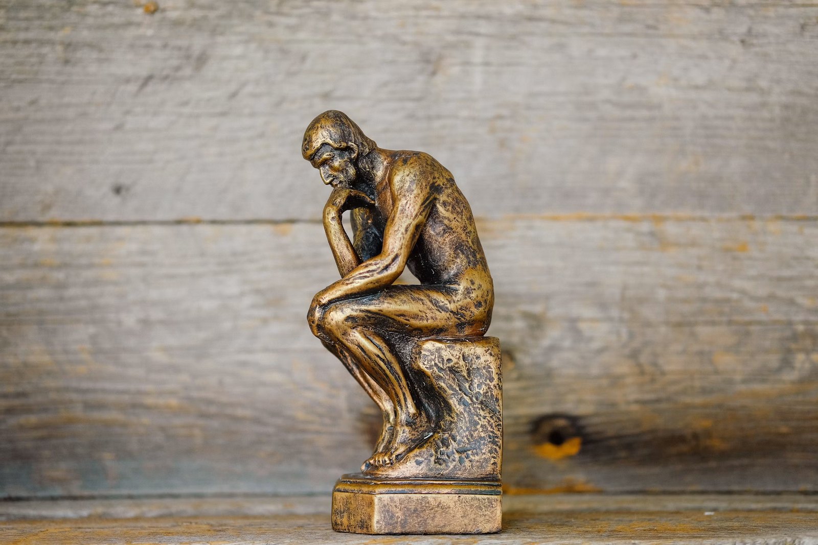A bronze statue of a seated figure resting its chin on its hand, deep in thought